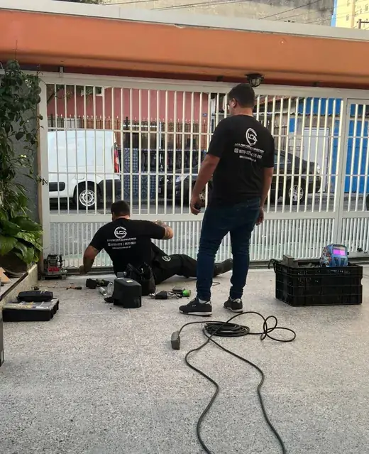Dois técnicos da LCA consertando o motor de um portão deslizante branco