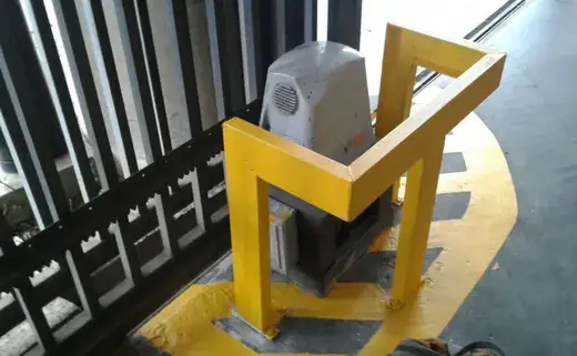 Motor de portão deslizante protegido por uma estrutura metálica amarela, ao lado da cremalheira